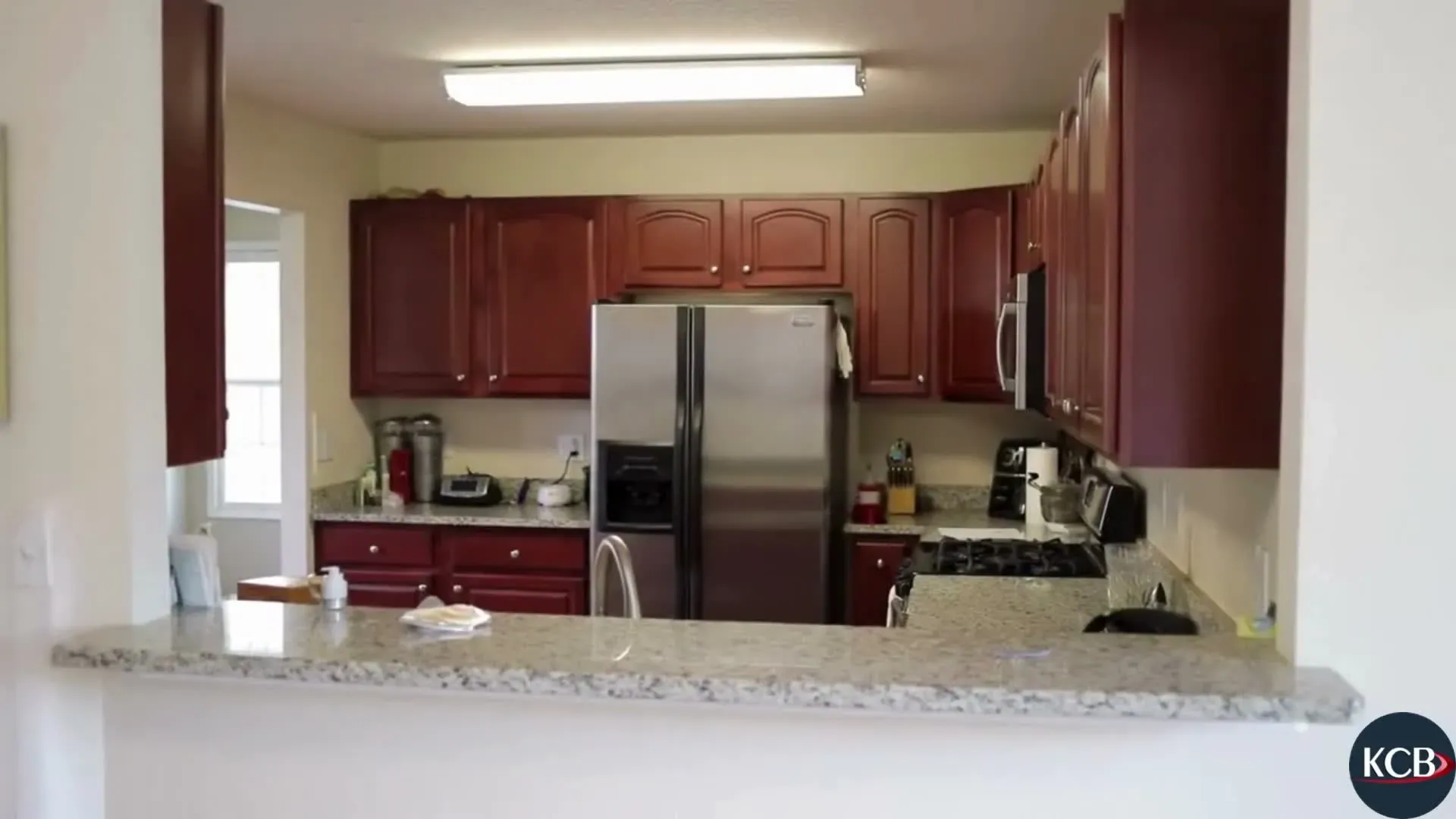 Kitchen with cherry-stained cabinetry, a stainless refrigerator and a granite-topped peninsula with seating