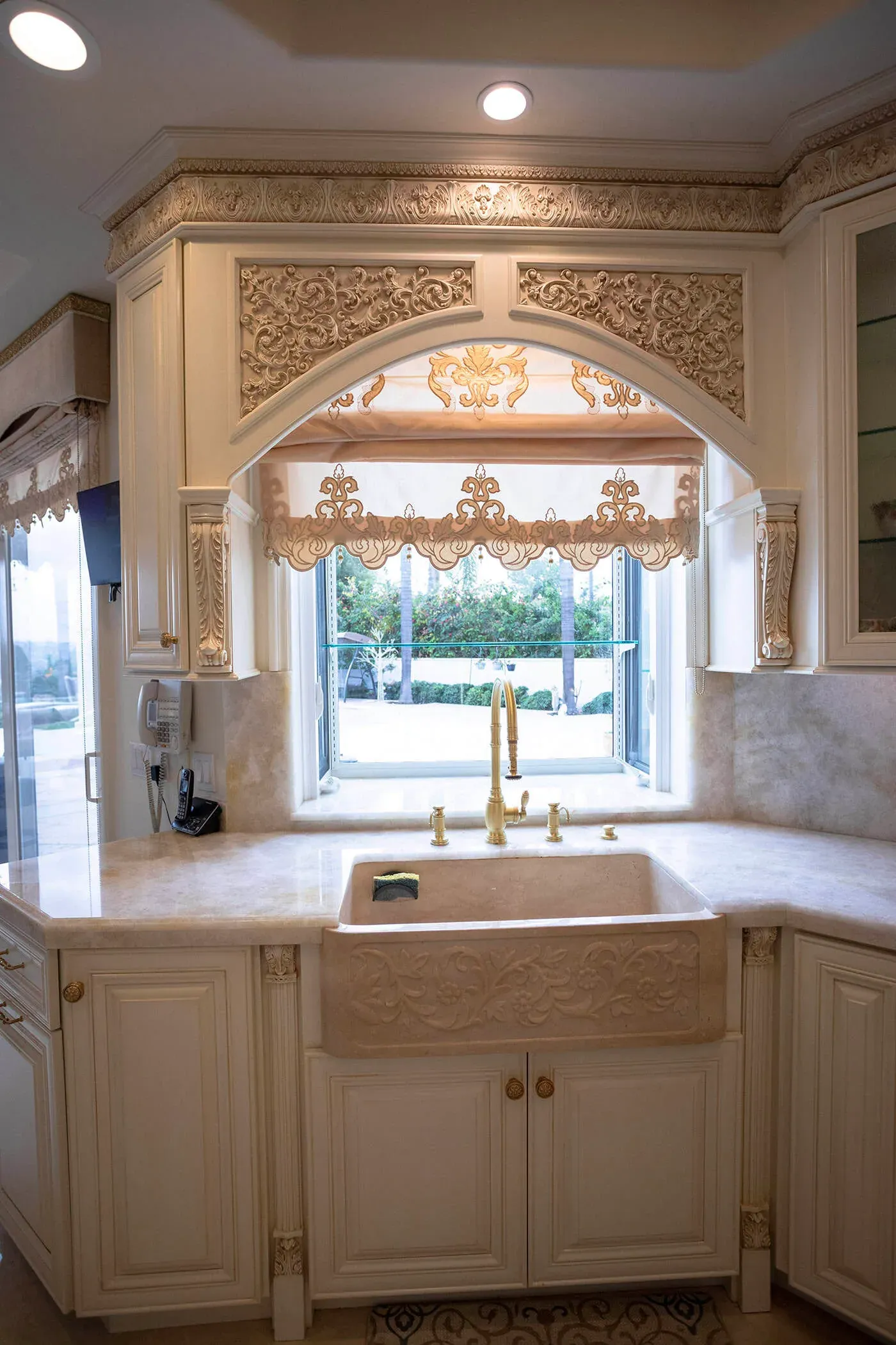 Farmhouse sink beneath an arched window with a shaped valance in a cream kitchen