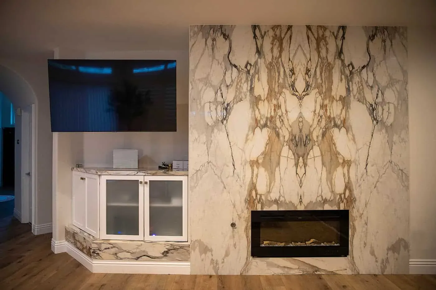 Book-matched white slab with dramatic gold and grey veining covering a fireplace wall around a linear fire
