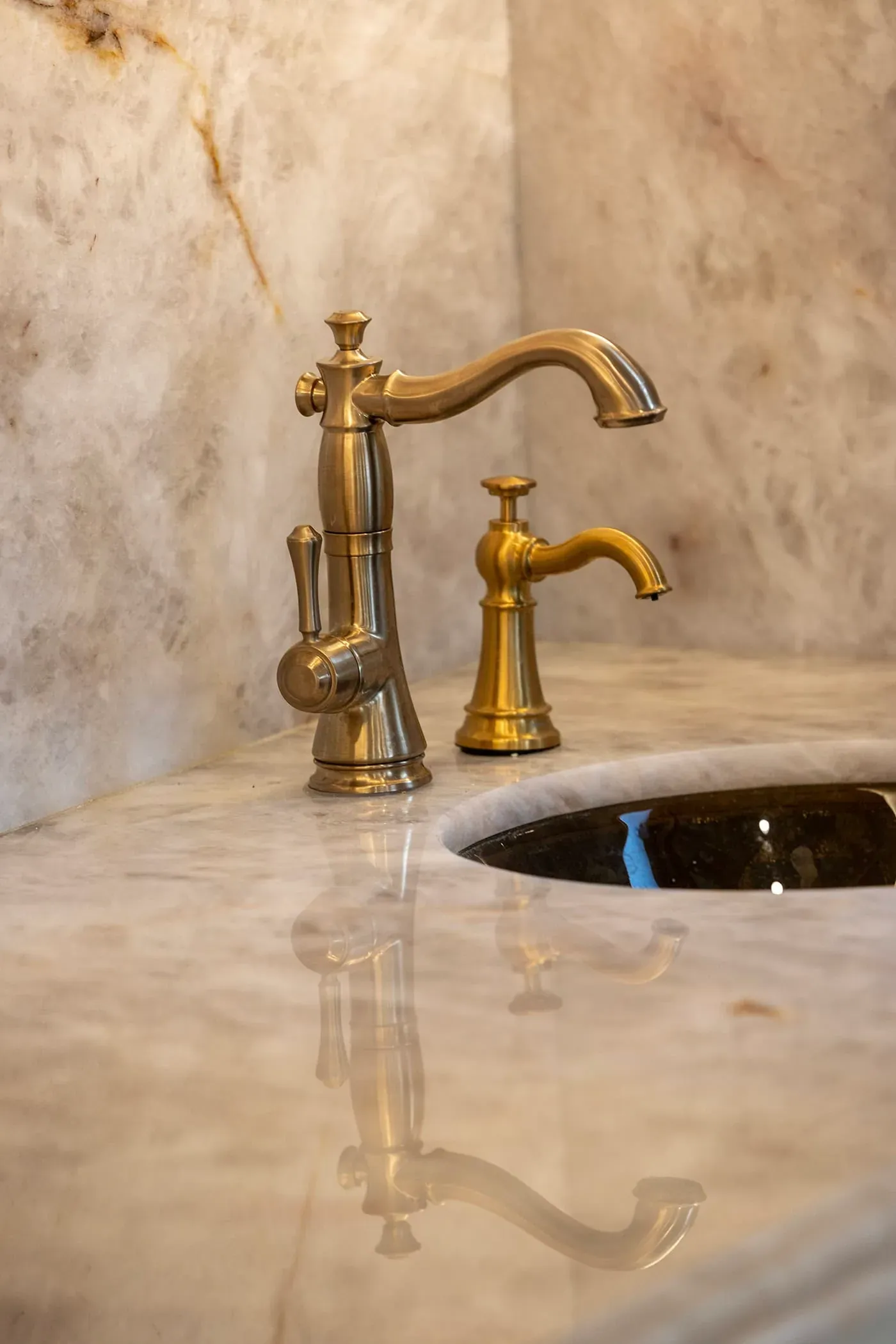 Polished onyx counter around an undermount sink with a brass bridge tap and a separate brass spout