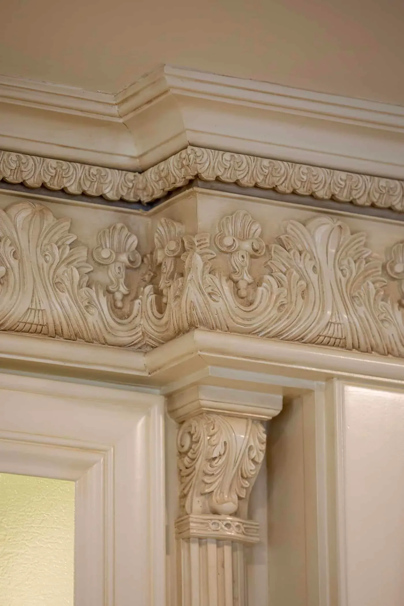 Carved acanthus leaf frieze running along the top of cream cabinetry beneath a moulded cornice