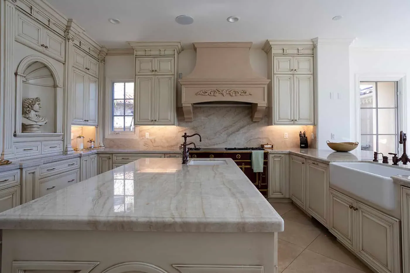 Newport Beach kitchen with carved cream cabinetry and an arched hood surround beside a marble island