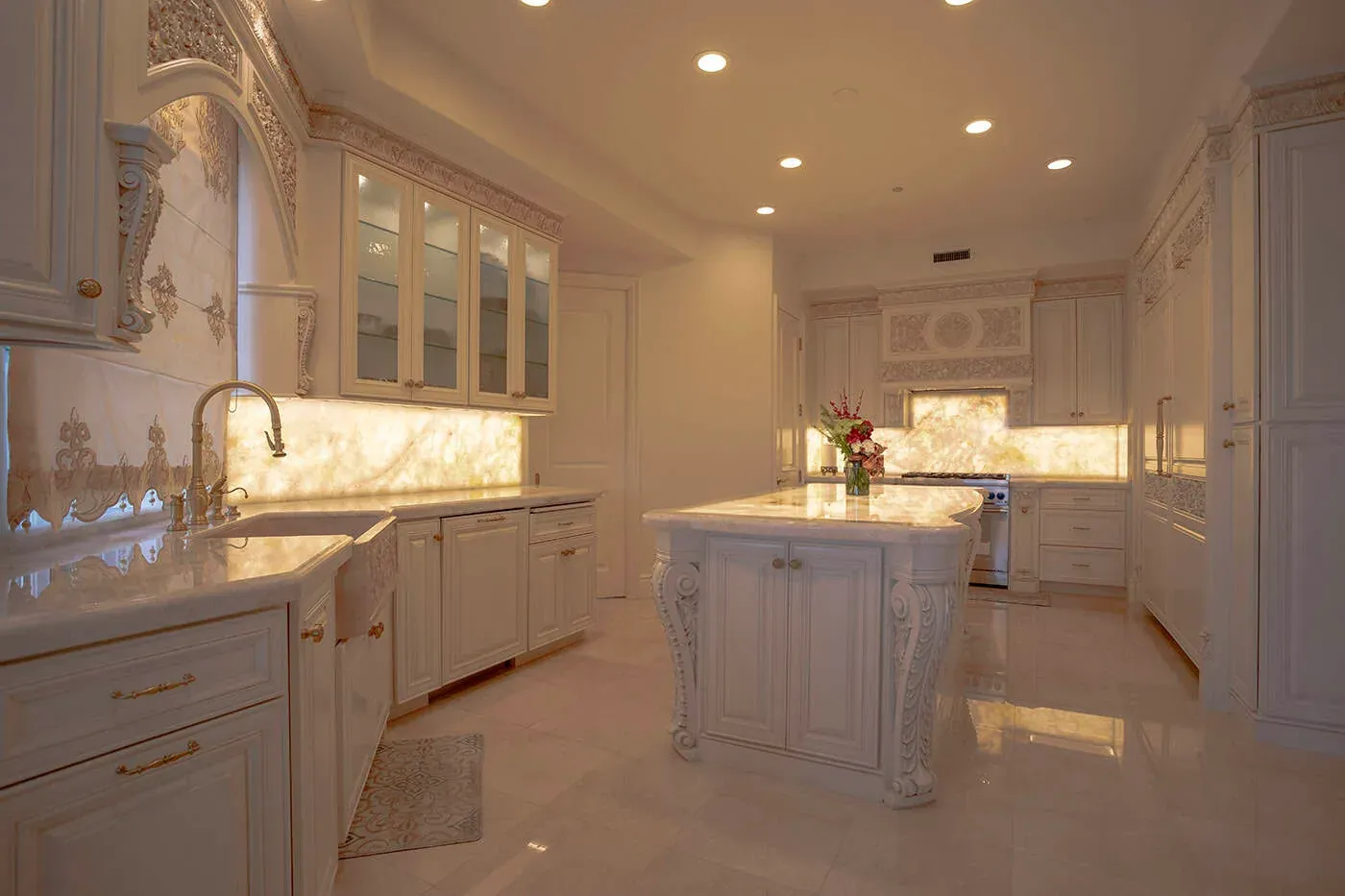 Laguna Hills kitchen with carved cream cabinetry, a backlit onyx backsplash and a marble island