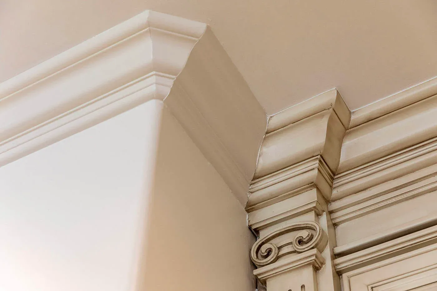 Glazed cream cabinet crown moulding meeting the ceiling above a carved scroll pilaster