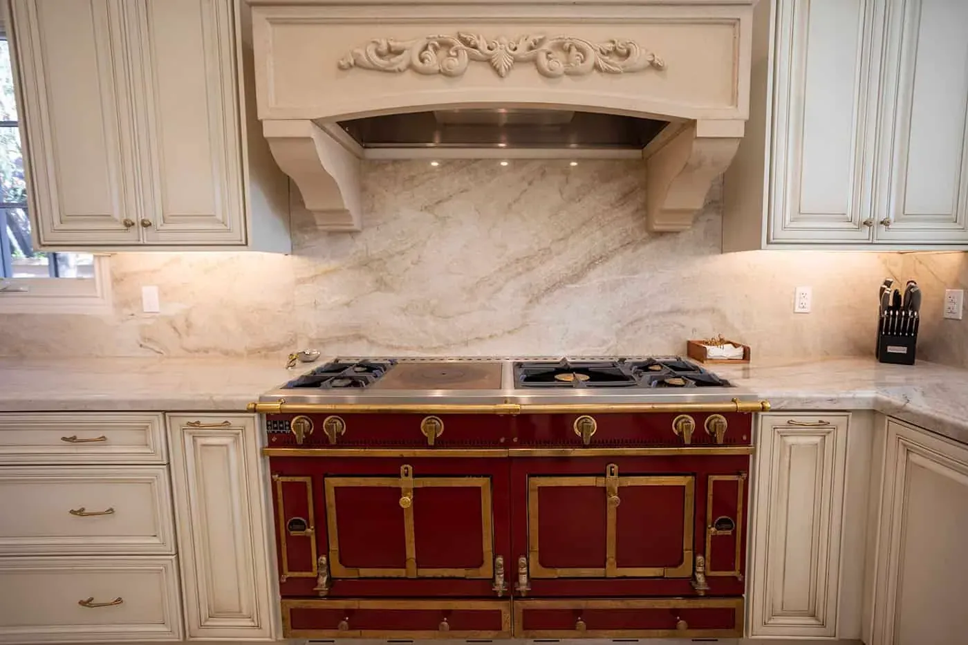 Carved hood above a red range with a stone slab backsplash