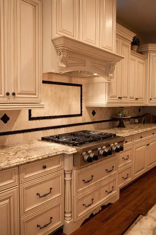 Carved hood over a stainless cooktop with a tiled backsplash inlay