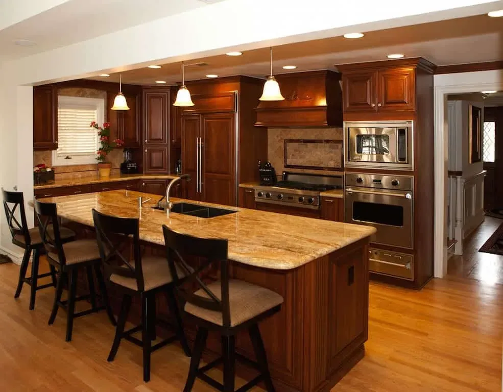 Honey-toned hardwood floor under a cherry kitchen with a granite island, bar stools and pendant lights