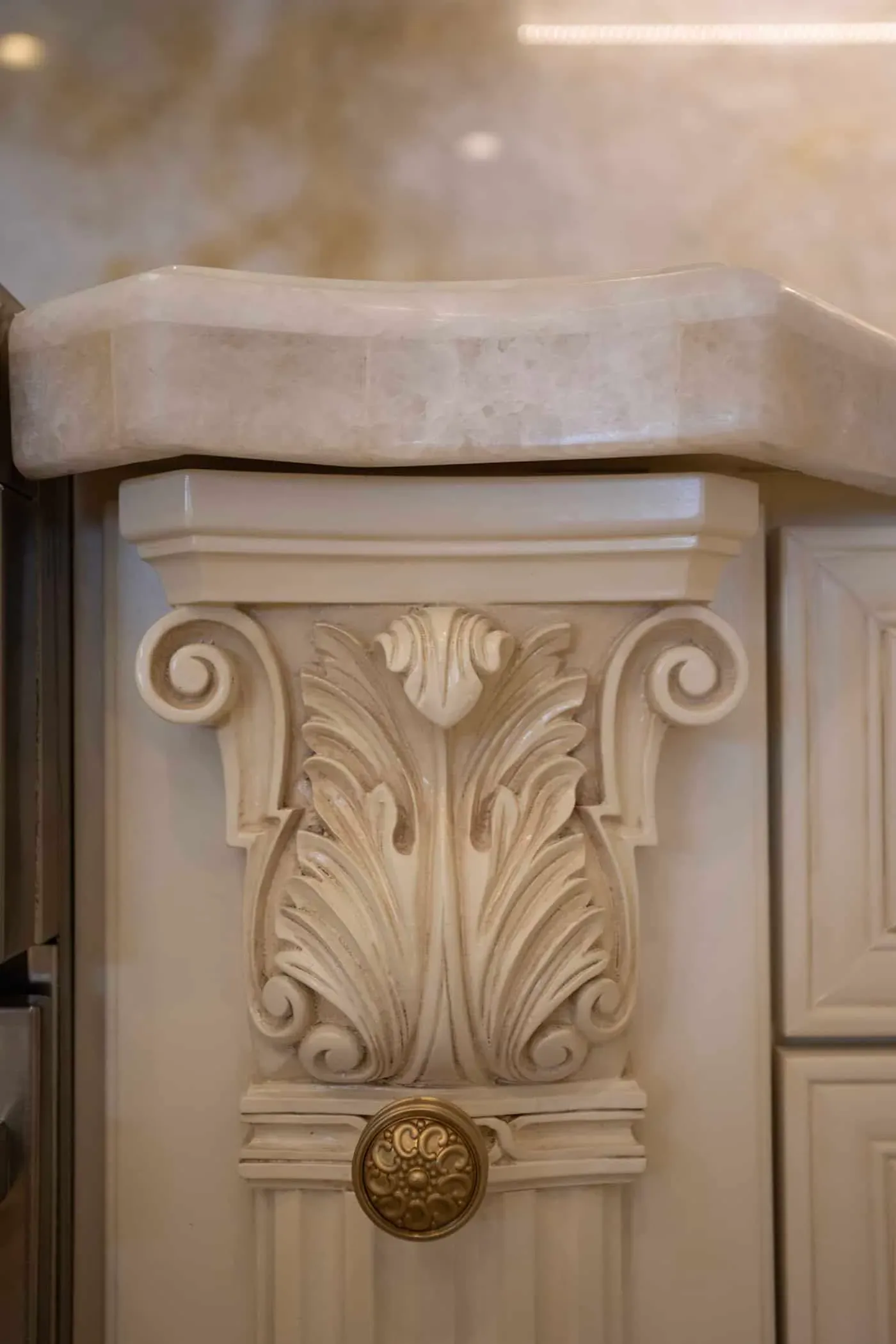Close view of a carved acanthus leaf corbel in cream with a brass knob beneath a polished stone countertop