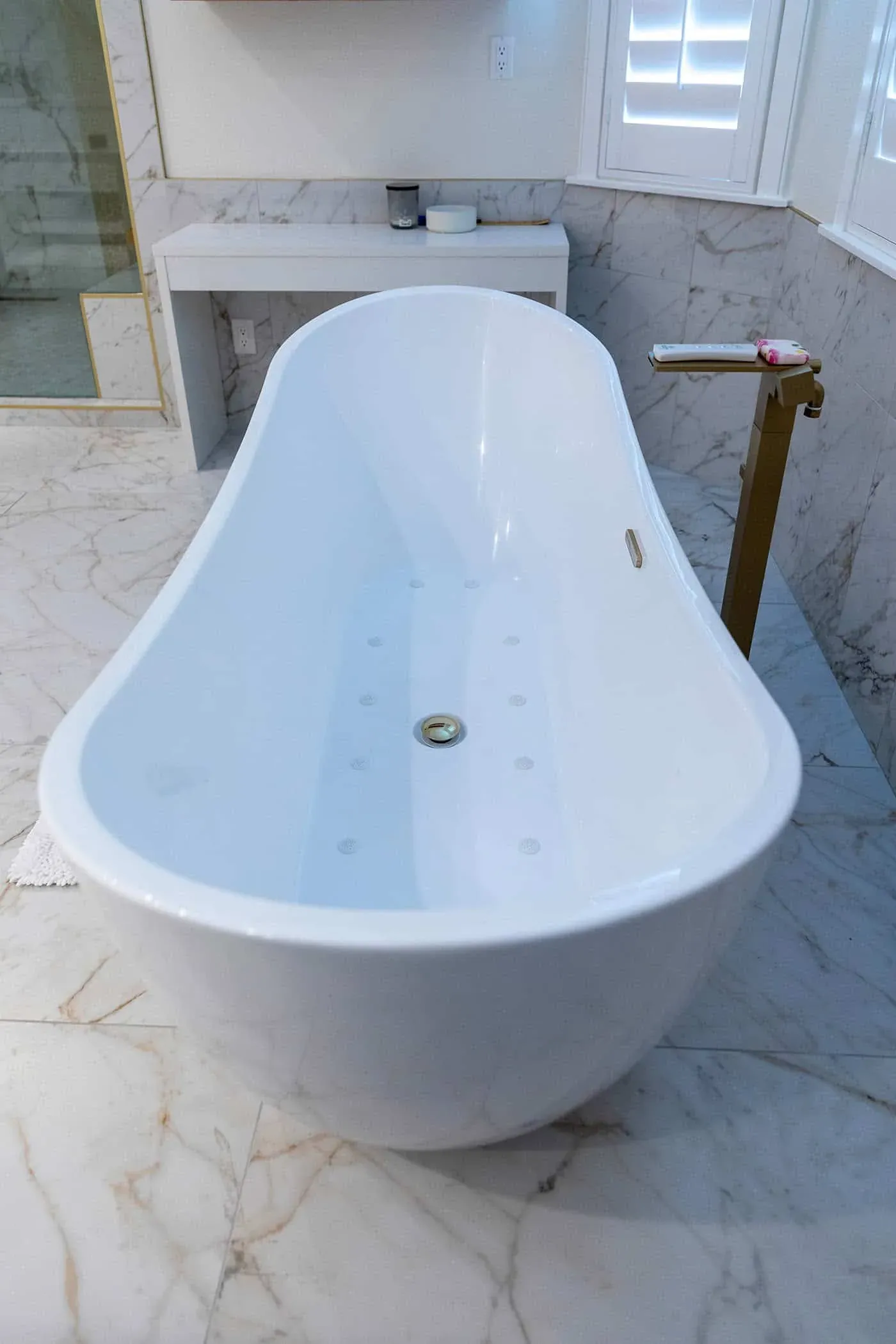 Freestanding tub with a brass floor-mounted filler on marble tile
