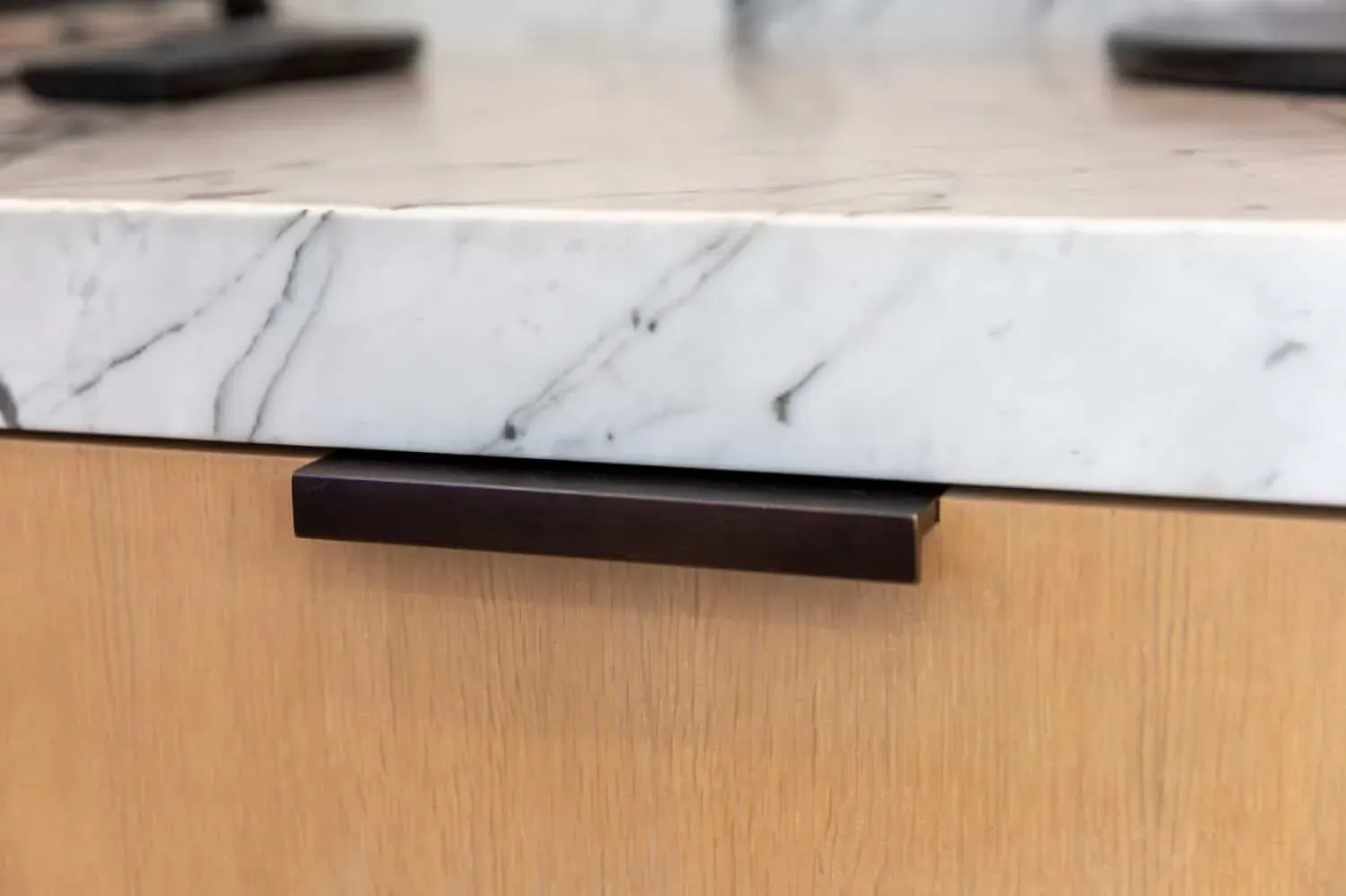 Close view of a veined marble worktop edge above an oak drawer front with a slim black cabinet pull