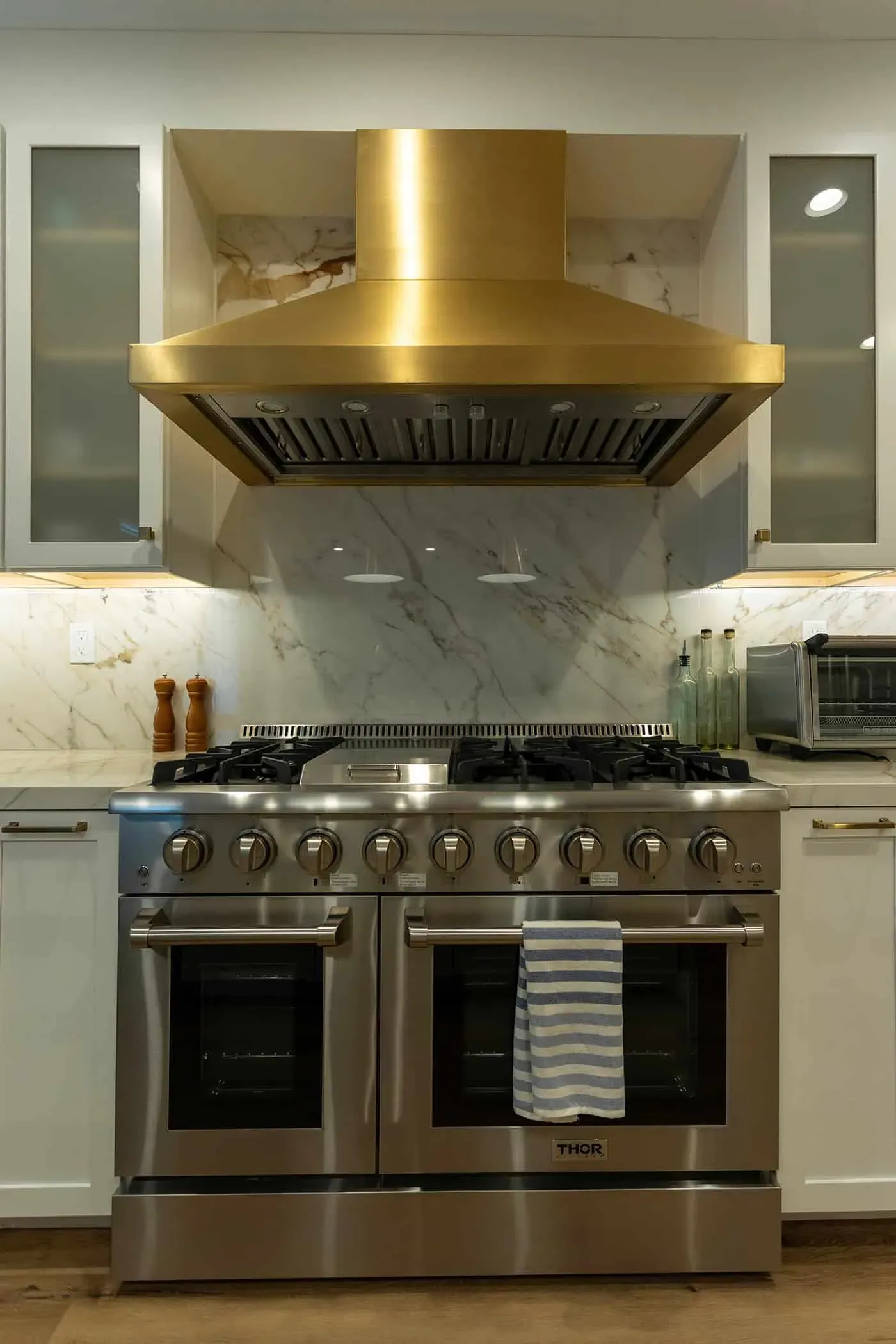 Professional range under a brass hood against a marble slab wall