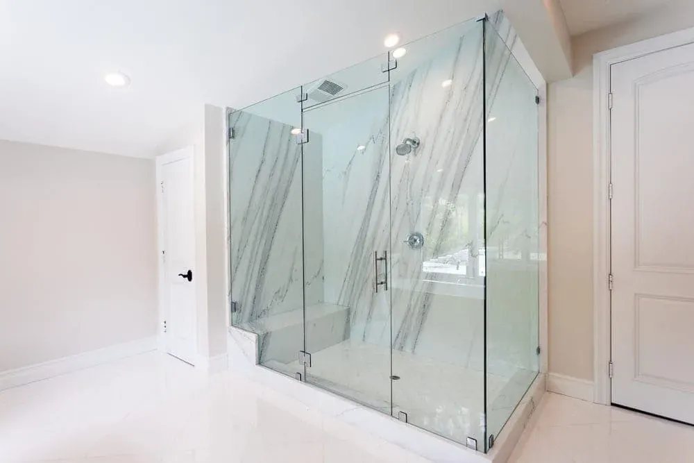 Corner frameless glass shower enclosure with full-height marble slab walls in a remodeled bathroom