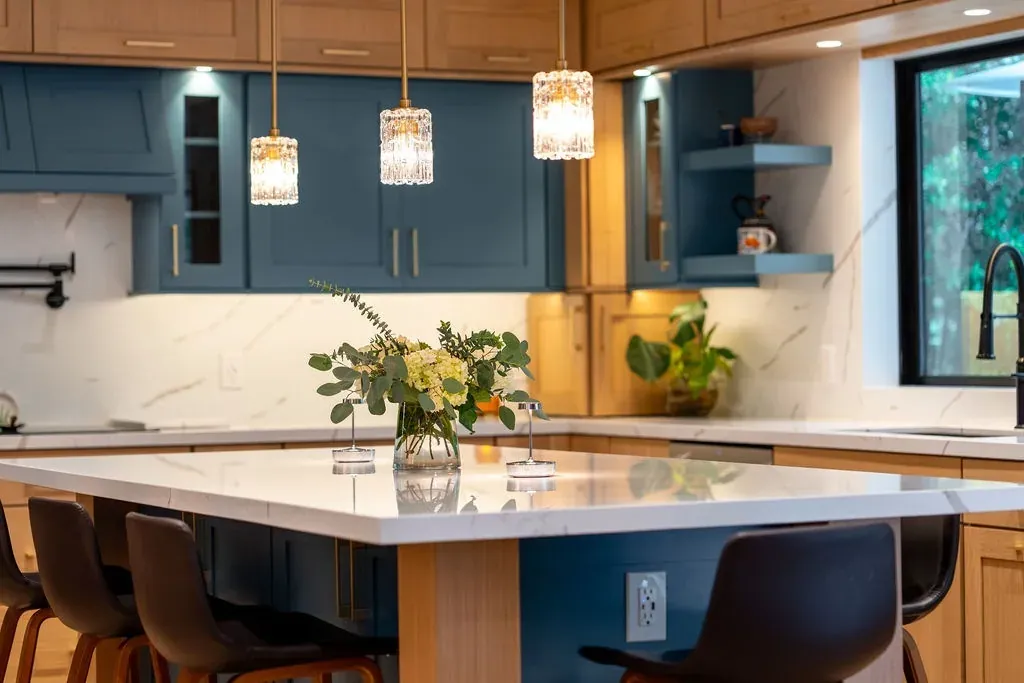 Three crystal pendant lights above a white quartz island with teal glass-front cabinets behind