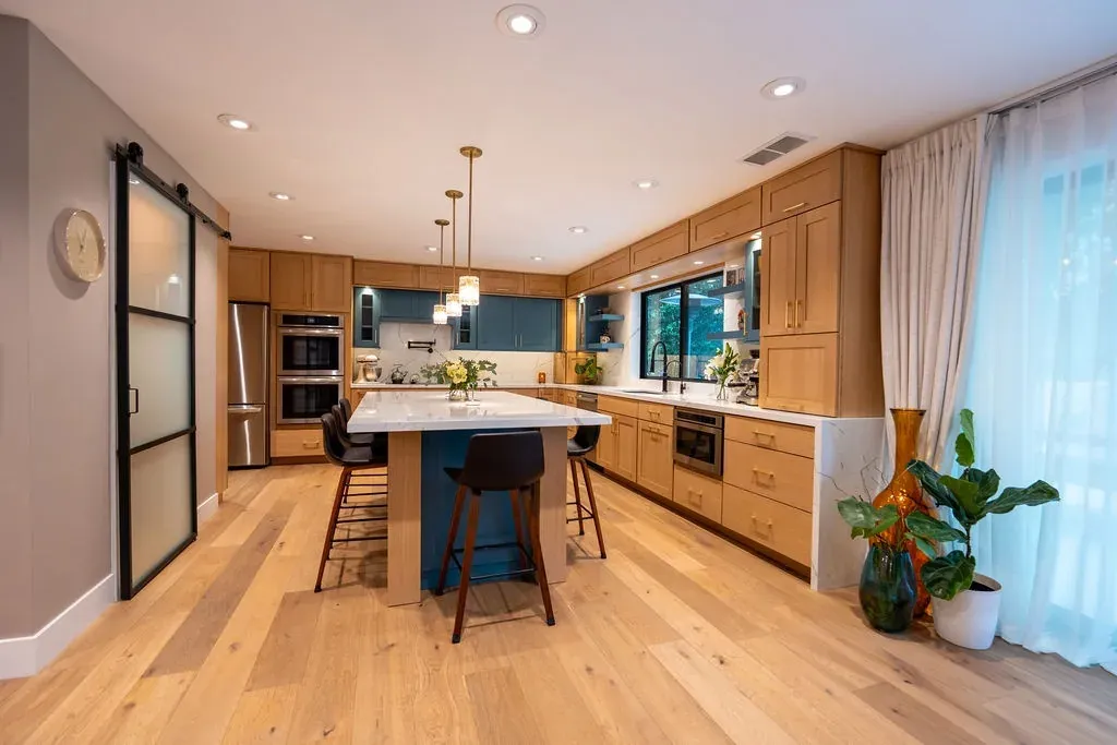 Kitchen with a black-framed frosted glass barn door to the pantry, oak cabinets and an island with four bar stools