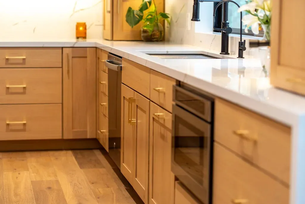 Run of natural oak base cabinets with brass bar pulls ending in a white quartz waterfall panel