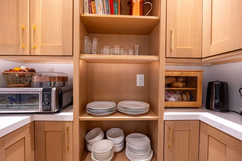 Walk-in pantry with oak shaker cabinets and open shelves holding plates, bowls and glassware