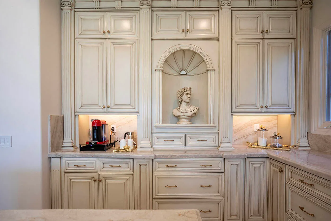 Cream cabinetry built around an arched display niche holding a classical bust above the counter