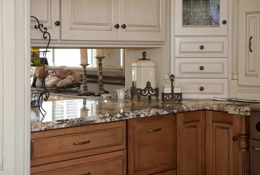 Speckled granite counters beneath a window over wood base cabinets with cream uppers