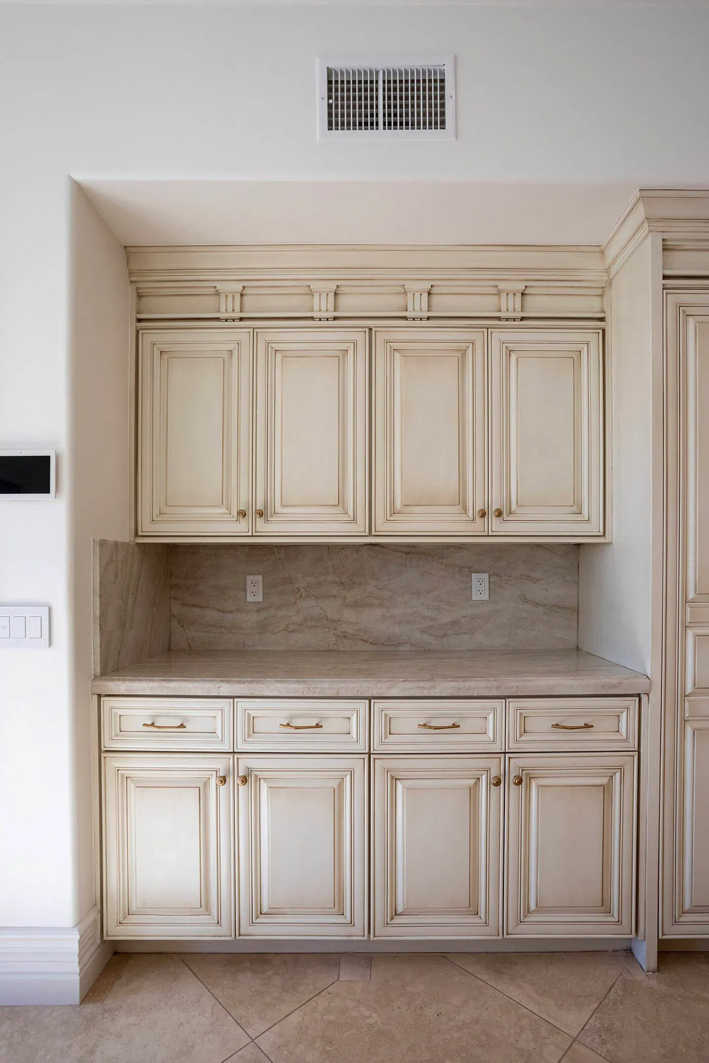 Cream glazed cabinetry above a stone counter and backsplash with an appliance garage run