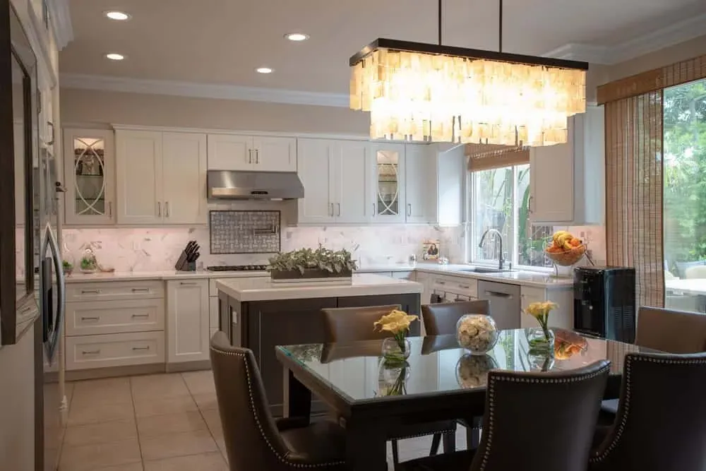 White kitchen that opens straight onto a dining table under a crystal pendant, with a dark island between them