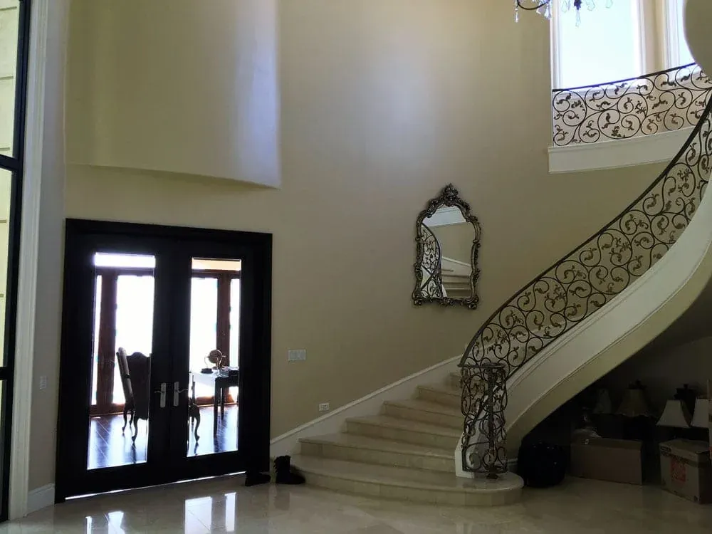 Two-storey entry hall with a curved stone staircase, a scrolled iron railing and dark double front doors