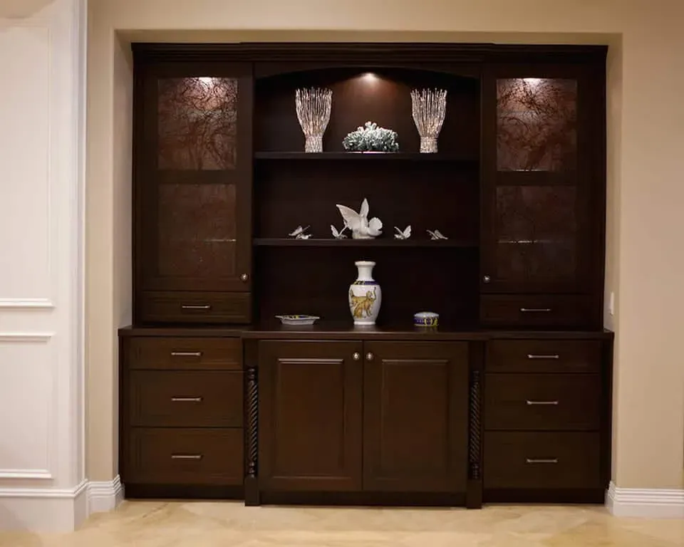 Dark stained built-in display cabinet with lit glass shelving above panelled base doors
