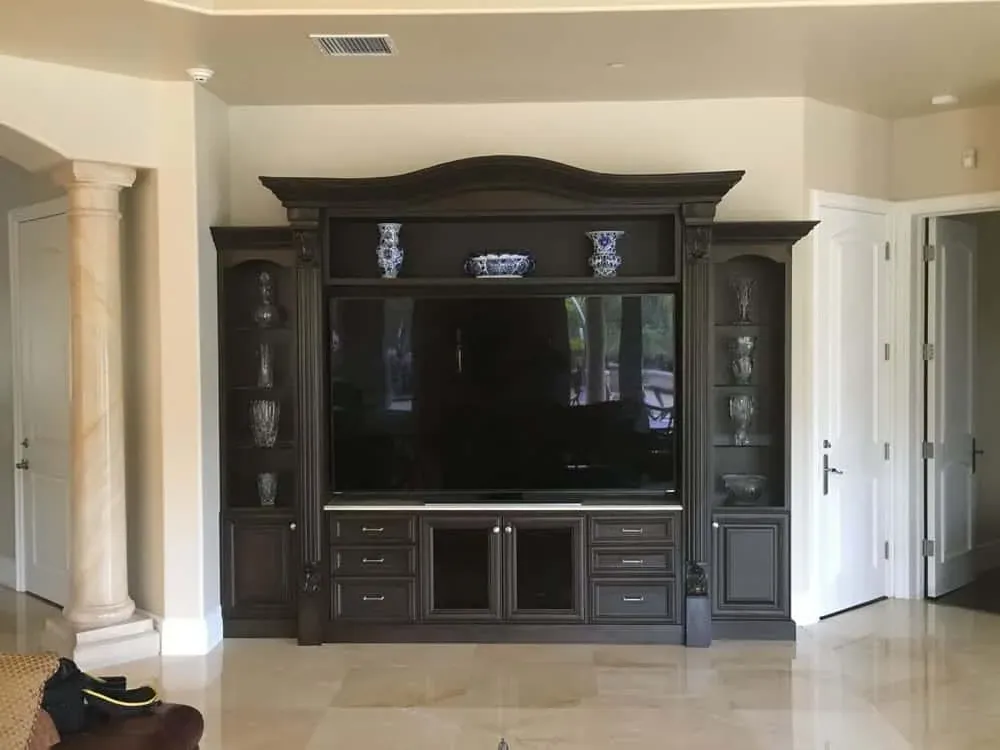 Dark built-in media wall with an arched crown, glass-front side cabinets and panelled doors below