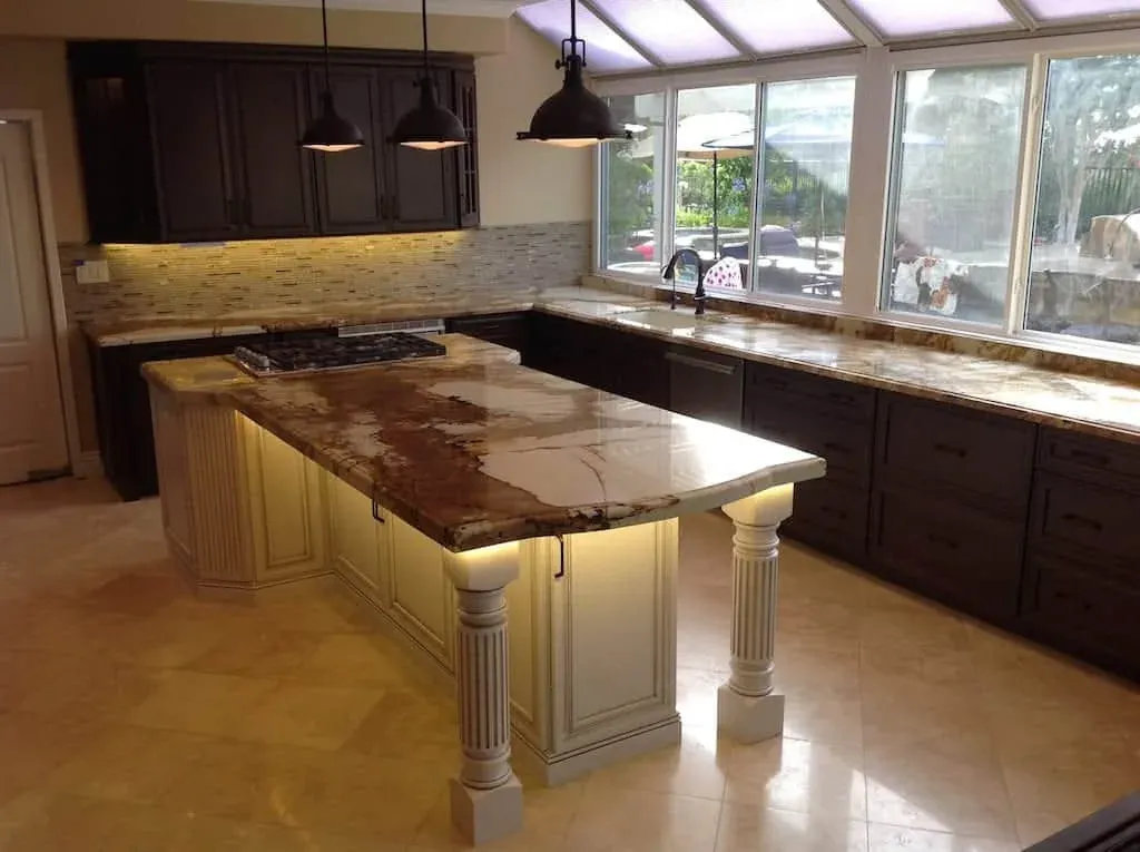 Dark perimeter cabinetry around a lit granite island on turned legs, with a wall of windows behind the sink