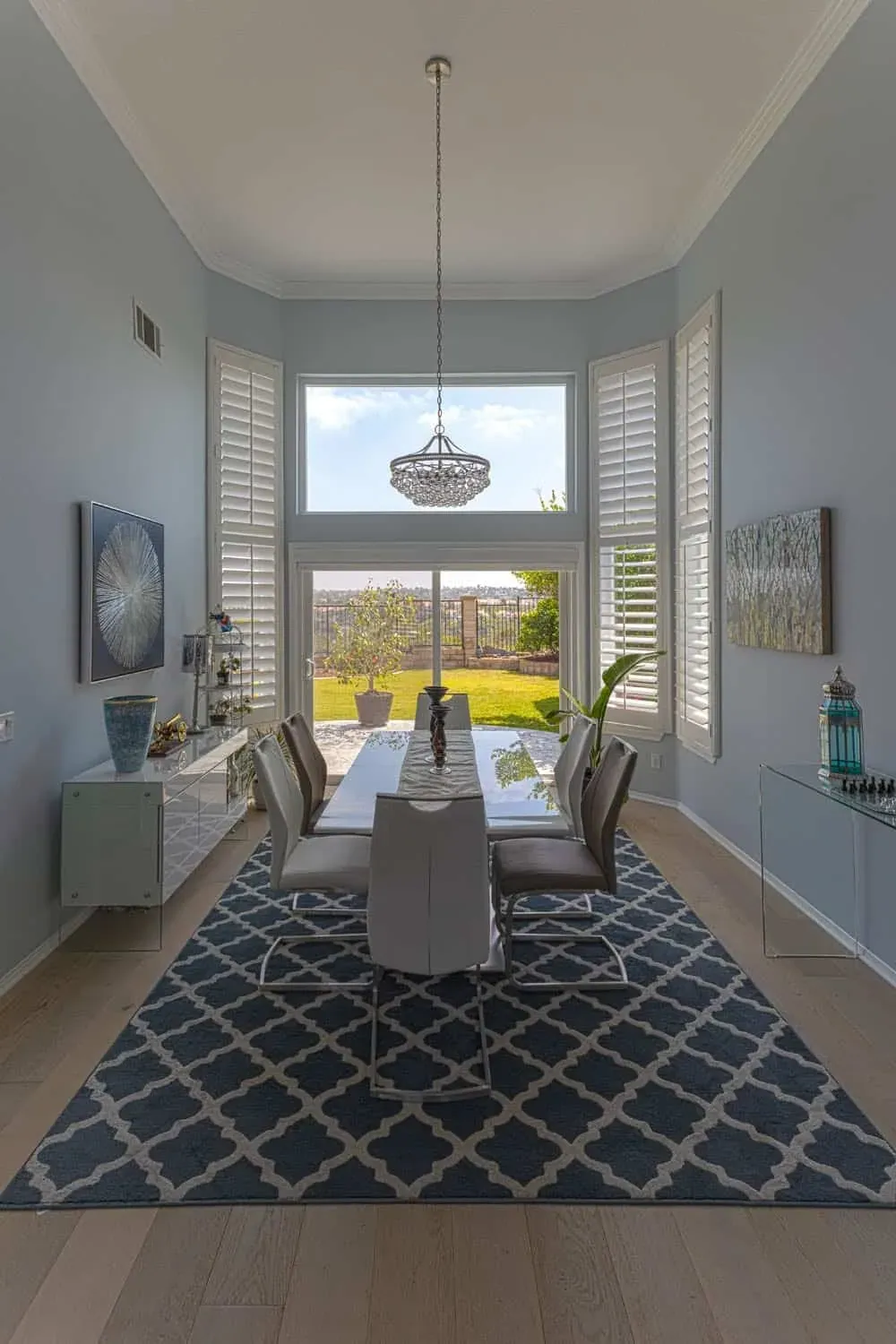 Light floor under a patterned rug in a dining room with a crystal pendant and tall shuttered windows