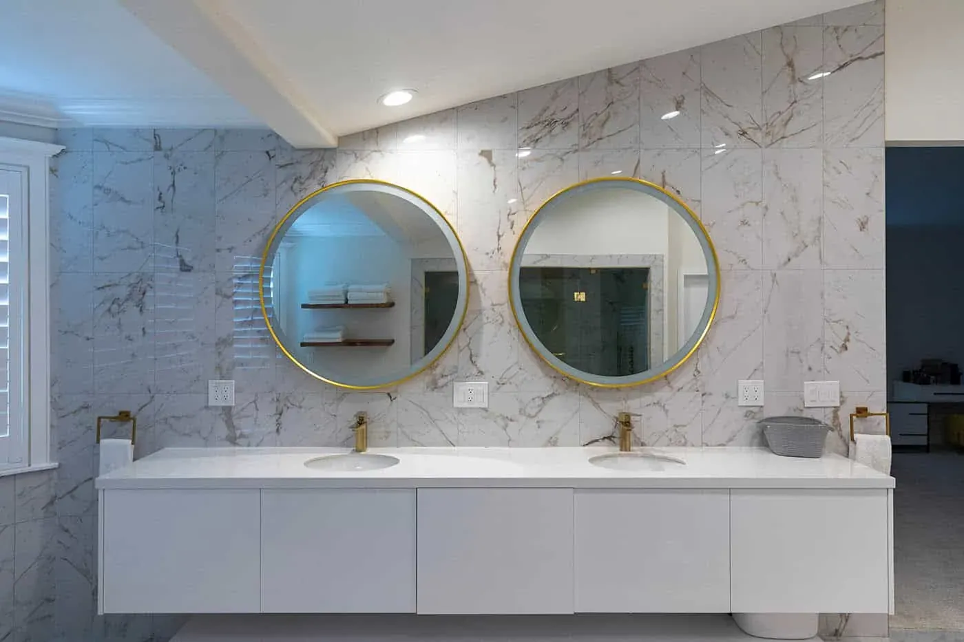 Remodeled bathroom with a double floating vanity, two round gold mirrors and marble walls