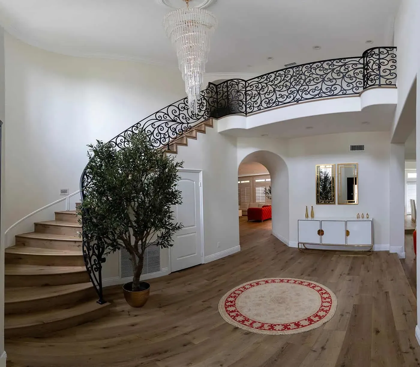 Wide-plank hardwood floor through an entry hall with a curved staircase, iron balustrade and round rug