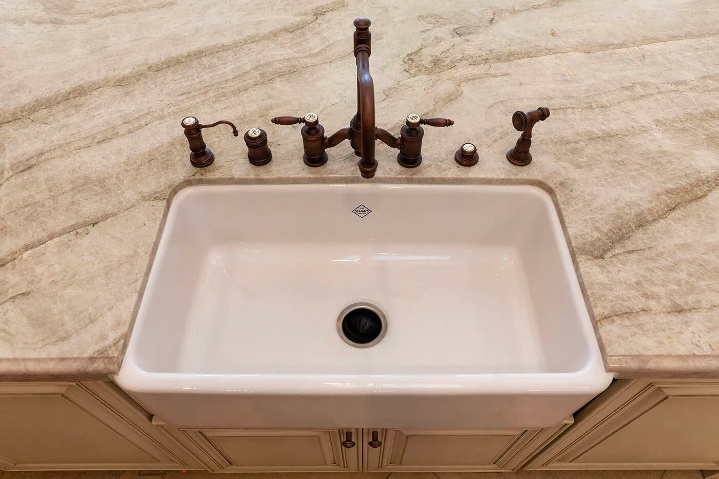 Farmhouse sink with a bronze bridge tap in a veined stone counter