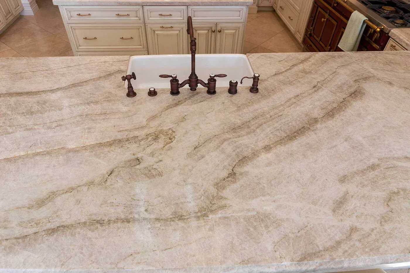 Veined quartzite worktop running up to a farmhouse sink with a bronze bridge tap
