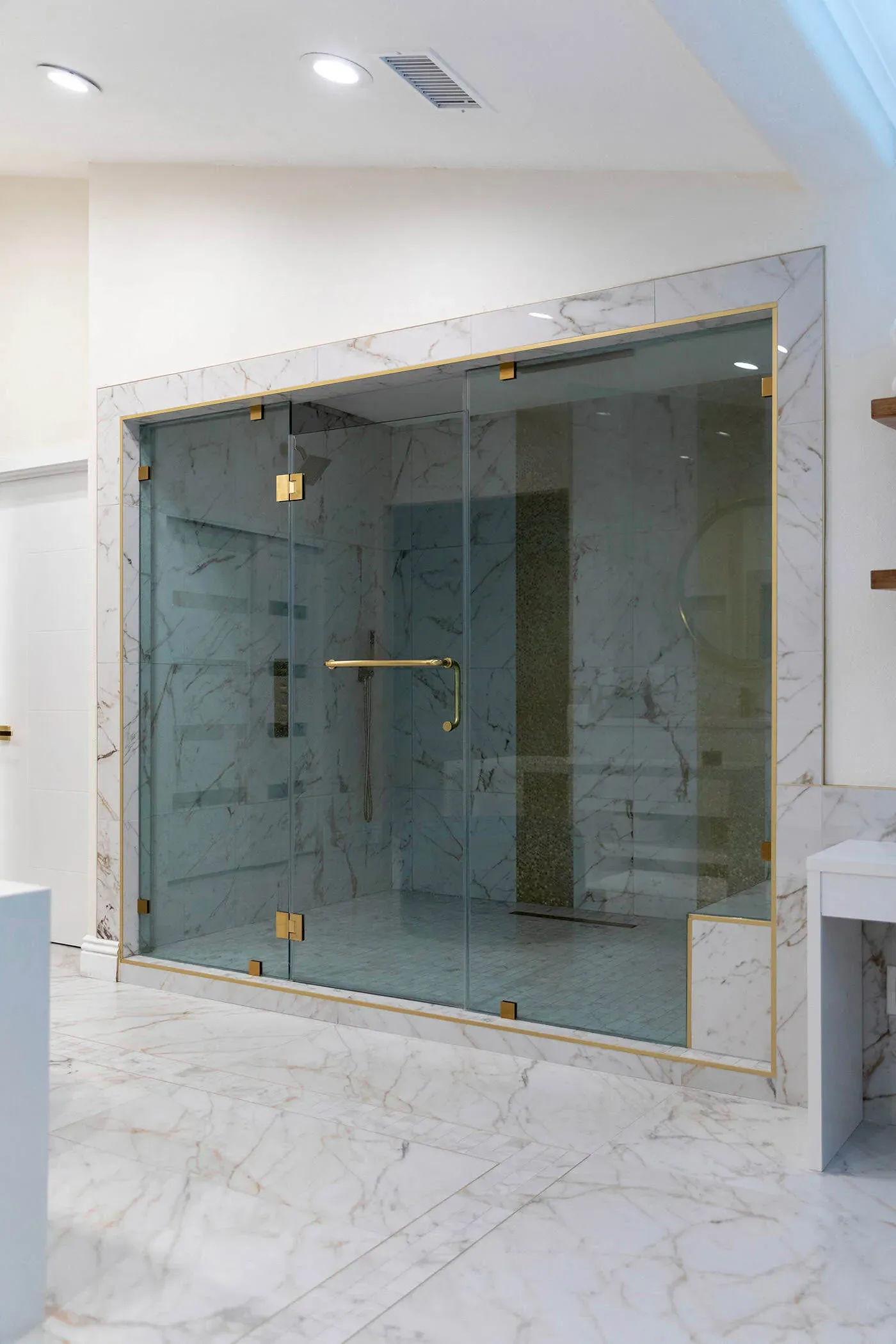Frameless glass steam shower enclosure with brass hardware and marble walls in a white bathroom