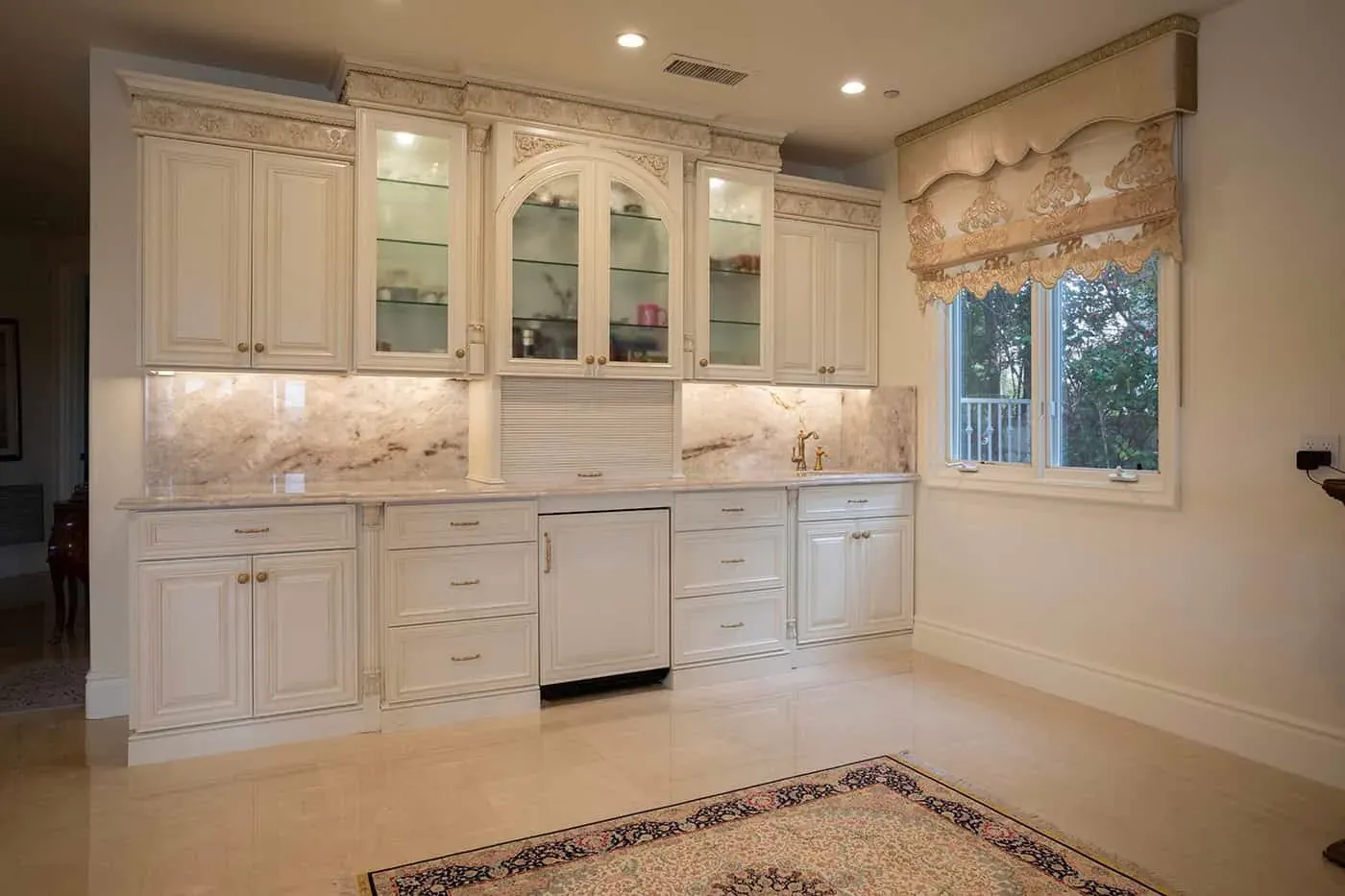 Polished stone floor tiles meeting the toe-kicks of cream glass-front cabinetry beside a window