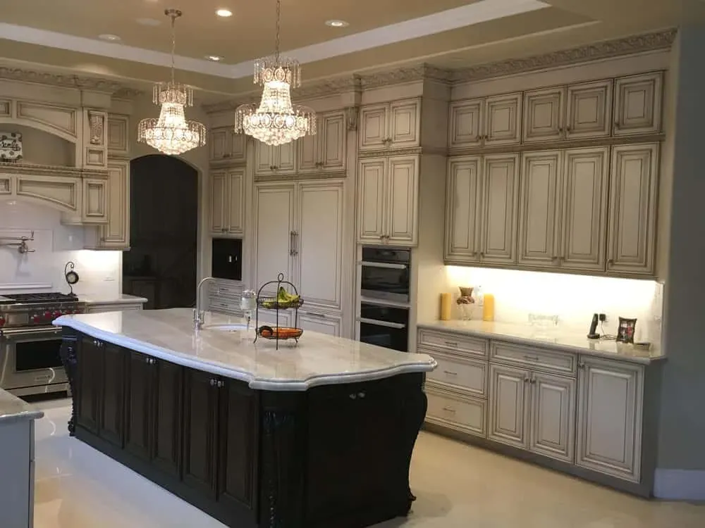 Glazed cabinetry and a dark island beneath two crystal chandeliers