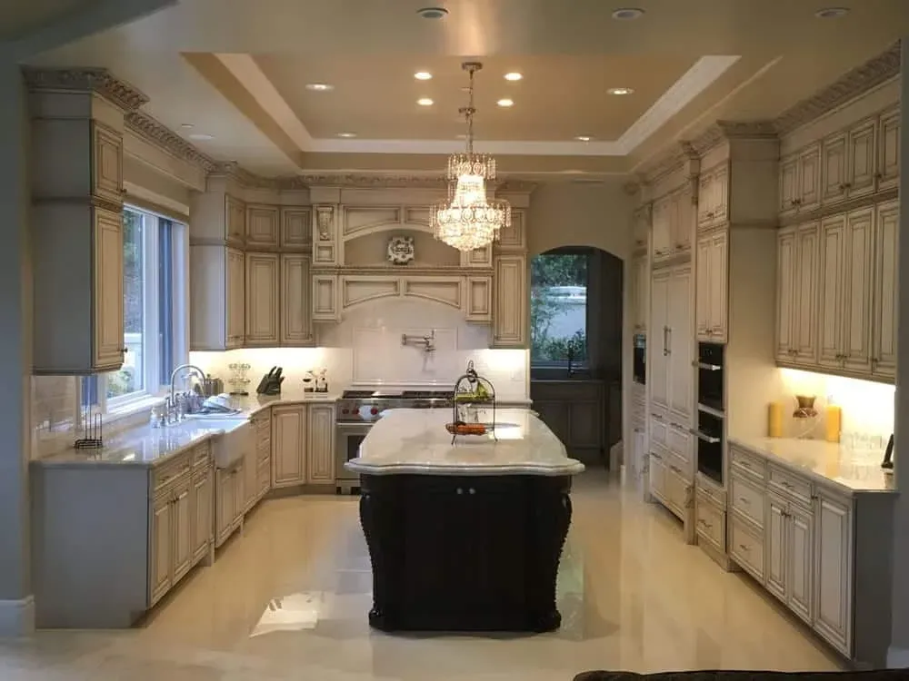 Glazed cream kitchen with a dark island, a crystal chandelier and polished stone flooring