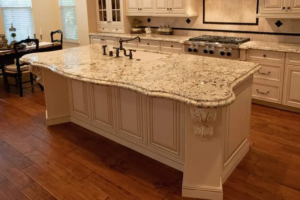 Cream kitchen island with a figured granite top, carved corbels and a bronze tap standing on a wood floor