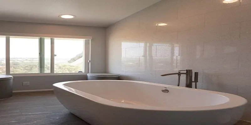 White freestanding soaking tub on a tiled floor beneath a row of bathroom windows