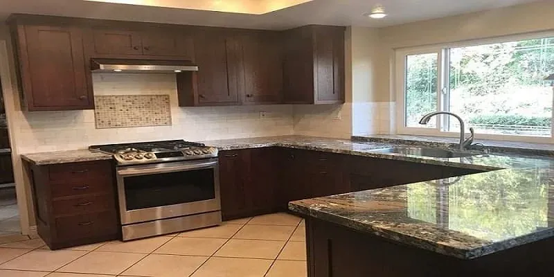 Dark wood kitchen with stainless gas range, mosaic tile backsplash, granite counters and a window over the sink