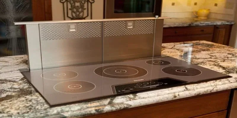 Stainless downdraft cooktop set into a speckled granite island countertop