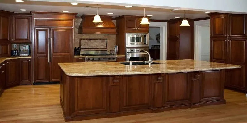 Cherry wood kitchen with a large granite-top island, dark upholstered chairs and hardwood flooring