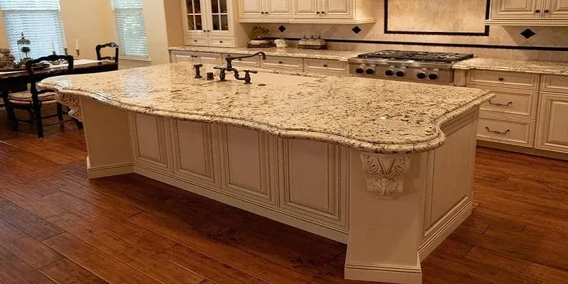 Cream kitchen island with a curved granite countertop edge, decorative corbels, a bridge faucet and wood flooring