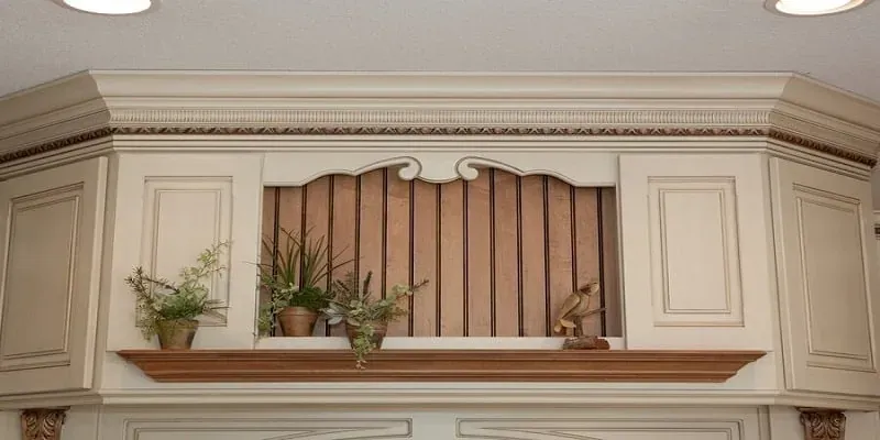 Close-up of cream cabinet crown molding with an open display shelf holding potted plants and a figurine