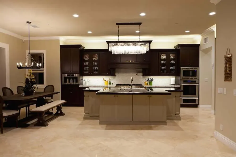 Dark espresso cabinetry with a large island, black granite counters, crystal chandelier and light tile flooring