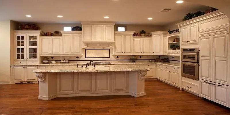 Cream cabinetry lines a kitchen with a large island, built-in fridge and warm wood flooring