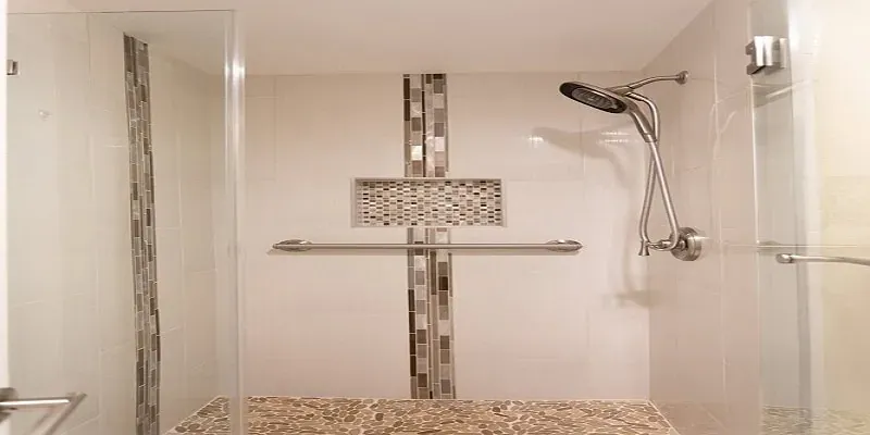 glass shower enclosure with a mosaic tile accent strip, handheld sprayer, grab bars and pebble-look floor tile