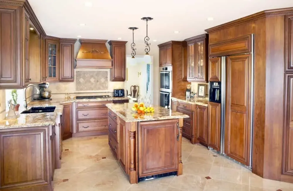 Honey-toned cherry kitchen with a centre island, pendant lights and a travertine floor