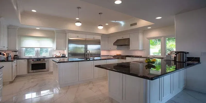 Bright white kitchen with a black granite island, pendant lights, stainless appliances and a polished stone floor