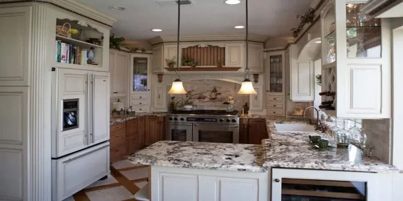 cream cabinetry with glass-front uppers, French door refrigerator and a granite-topped island with carved wood hood